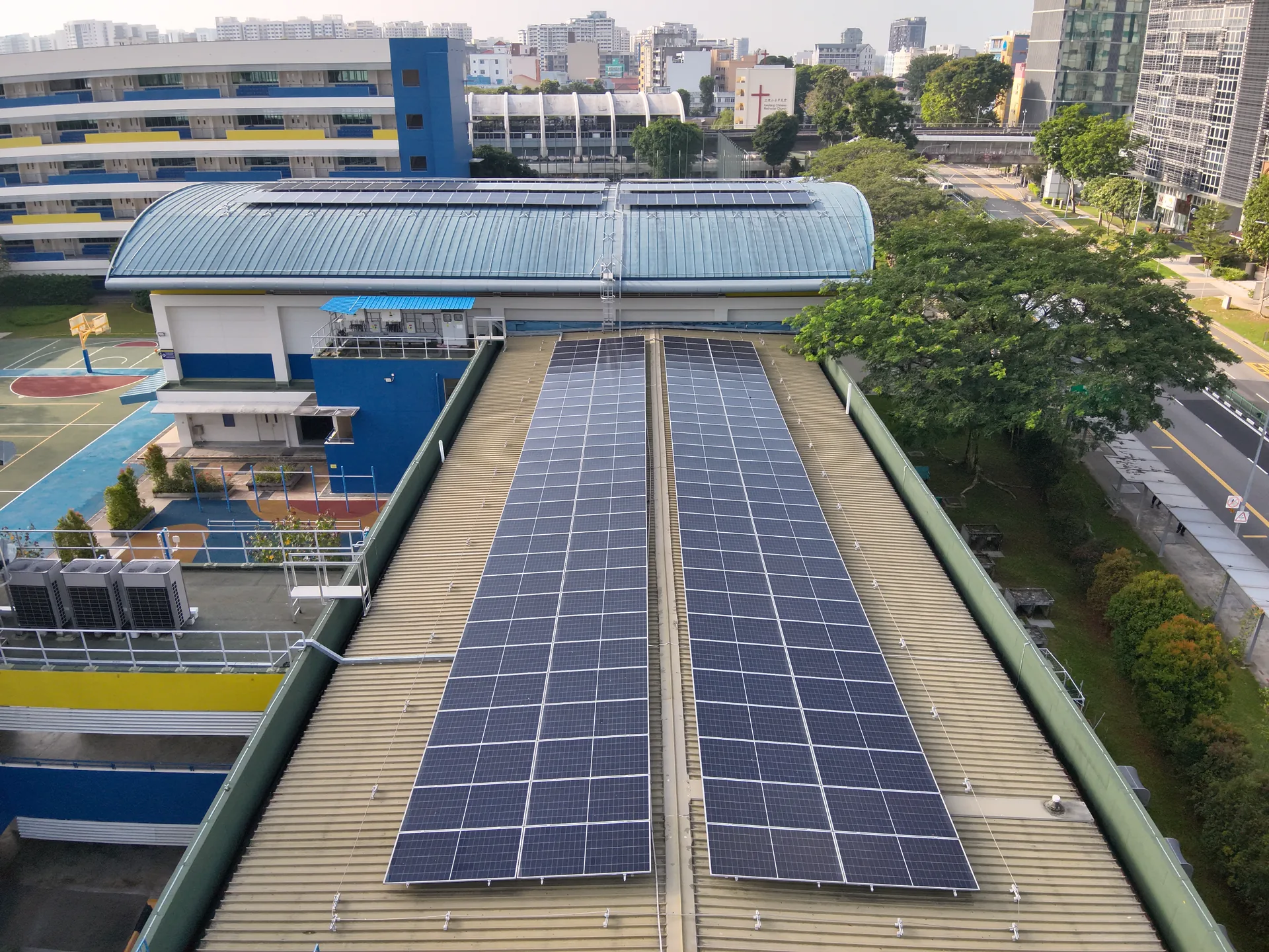 MOE schools estate, Geylang Methodist Sec School curved-roof PV array with sports field and Singapore skyline
